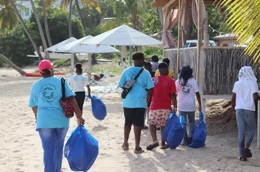 Volunteers carrying blue waste bags along the beach.
